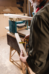 partial view of woodworker measuring plank near thickness planer.