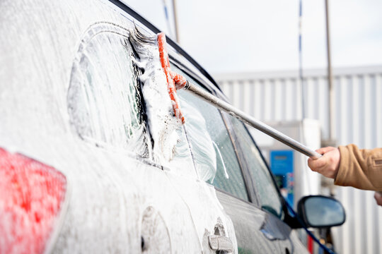A close up photo of washing a car with a brush and soap foam before cleaning it with a jet wash in the open air. Cleaning and disinfection. Security measures during the epidemic