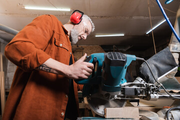 low angle view of carpenter cutting timber with miter saw.