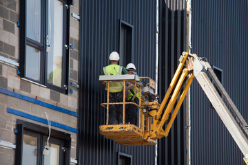 Naklejka premium Builders working off Telescopic Boom Lift while fitting insulated sandwich panels to the facade of a new multistorey residential building. Working at height safely