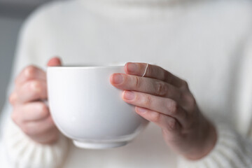 close up of woman's hands holding a big white cup of hot tea 