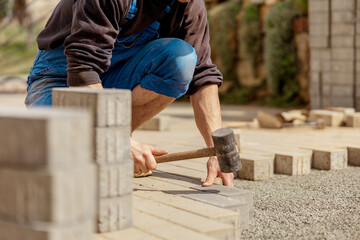 Young man laying gray concrete paving slabs in house courtyard on gravel foundation base. Master...