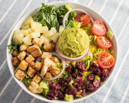 Guacamole Salad with Pineapple, Cranberries, Red Onions, Croutons, and Lettuce in a Bowl on a Linen Tablecloth