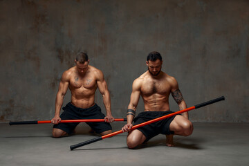 Two men aikido fighters with wooden fight stick posing in studio, fight demonstration