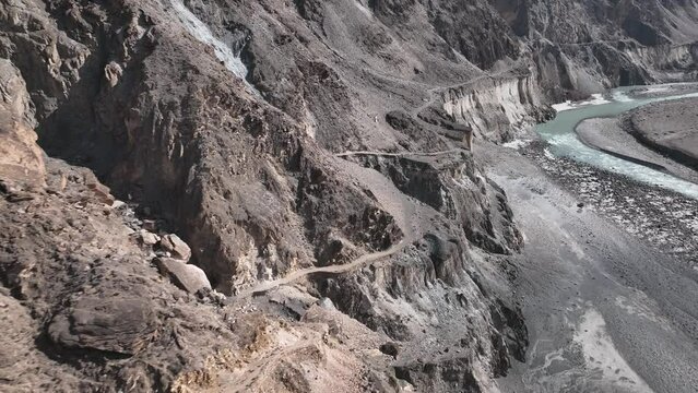 Aerial View Of Winding Old Silk Road Through Rugged Arid Mountains Beside River