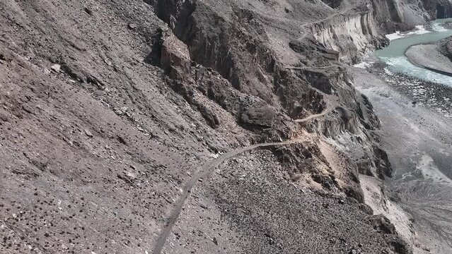 Aerial Remote Surveillance View Of Winding Old Silk Road Through Rugged Arid Mountains Beside River