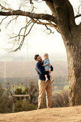 Fototapeta premium a cute father with a beard plays with his little daughter on a swing which is on a hill overlooking the city. early spring. games with father.