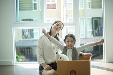 Happy Asian girl playing with cardboard boxes and her bear, having fun while moving new home.