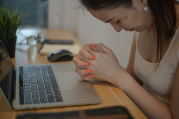Woman hands pray with cross, bible and laptop at home.