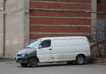 Old rusty white minivan parked at a brick house walls, Kollontai Street, St. Petersburg, Russia,...