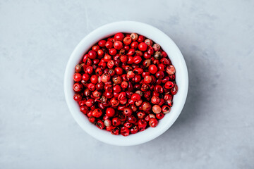 Pink peppercorn in white bowl on gray stone concrete background