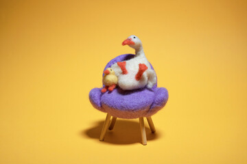 Needle felting duck sitting on a chair with yellow background.