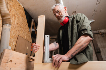 low angle view of furniture designer measuring wooden details in woodwork studio.
