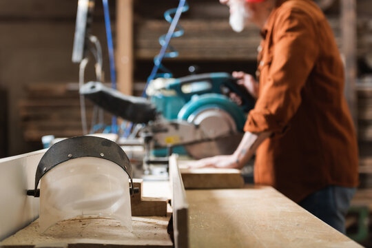 selective focus of face shield near cropped carpenter working on blurred miter saw.