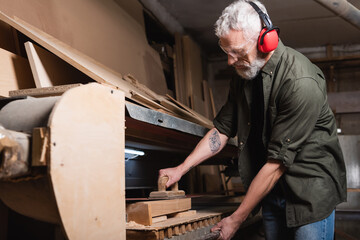 bearded woodworker polishing board in sander machine.