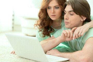 Portrait of happy young couple looking at laptop while lying on floor