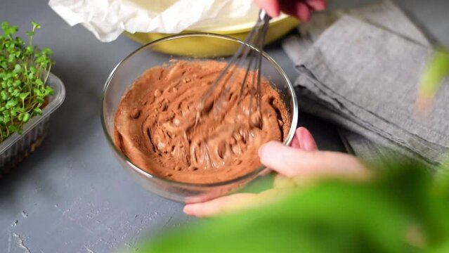 Making liquid chocolate dough for cake, pancakes or pie. Stirring batter and cocoa powder with a whisk in the glass bowl. Preparing a dessert