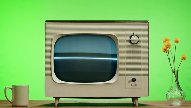 Old television with grey screen on chroma green background. Close-up of vintage tv on table with retro phone, nostalgia. 