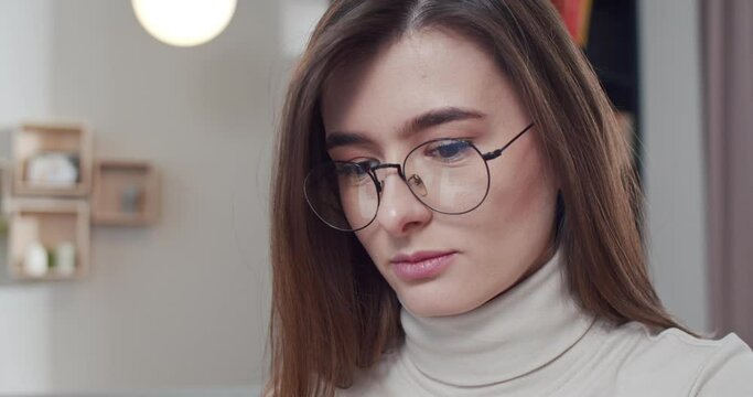 Close up of beautiful young Caucasian female freelancer or student indoor. Pretty woman face in glasses at home while working. Work at computer. Workday.