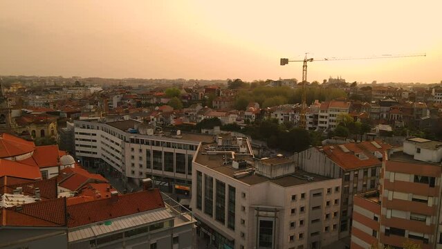 Downtown Buildings Rooftop And Construction Crane In The Background With Warm Sunset Sky In Porto, Portugal - Drone Shot