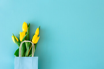 Flat lay blue background with yellow tulip flowers in a paper bag.