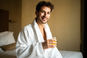 Portrait of h young man in white bathrobe drinking orange juice