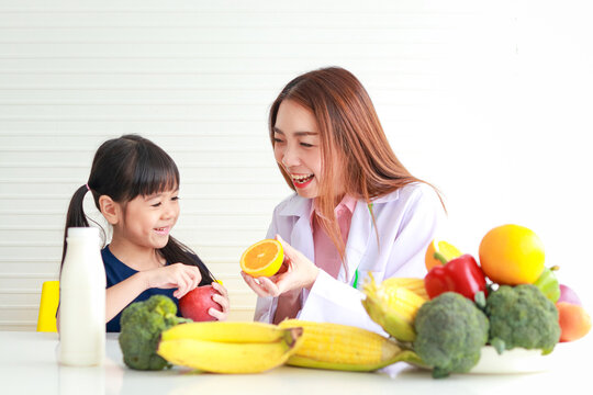 Nutrition For School-age Children. A Beautiful Nutritionist Or Doctor Explains The Benefits Of Fruits And Vegetables To A Little Girl. Choosing The Right Food According To The Age Of The Child.