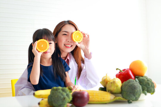 Nutrition for school-age children. A beautiful nutritionist or doctor with a little girl holding an orange. Choosing the right food according to the age of the child for good health - Powered by Adobe