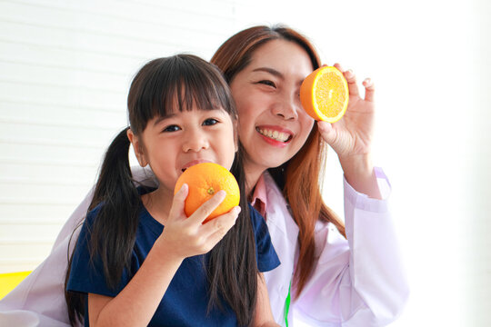 Nutrition for school-age children. A beautiful nutritionist or doctor with a little girl holding an orange. Choosing the right food according to the age of the child for good health - Powered by Adobe