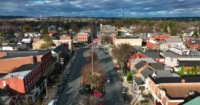 Anytown USA on bright sunny day under dramatic clouds and sky. Town square with businesses and car traffic. Bare trees, late winter, early spring season.