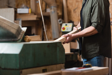 partial view of carpenter with plank working on thickness planer in workshop.