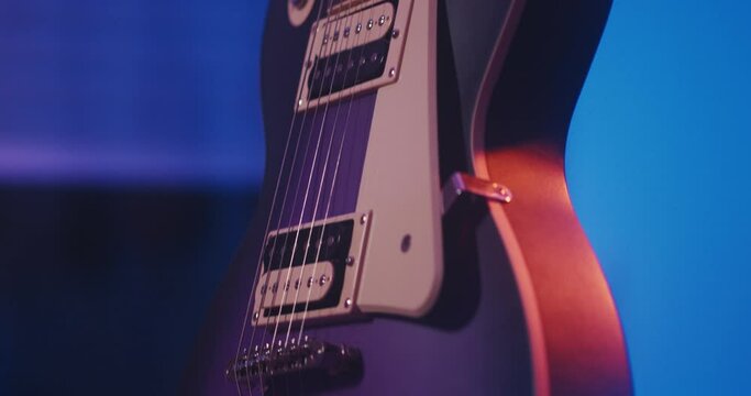 Panning up on a purple Les Paul electric guitar with a white pickguard illuminated by a moody blue-organge backlight.