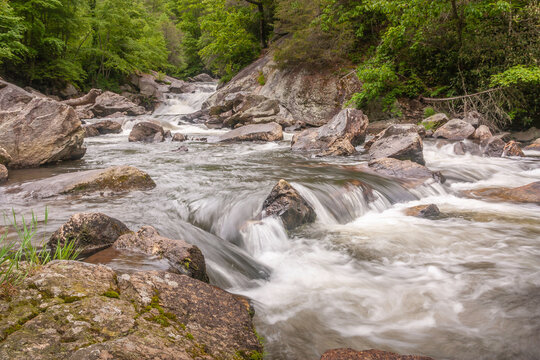 Beautiful photo of water Cascading out from between trees over and around boulders late overcast day. In the Cullasaja River alone US 64 west of Highlands NC, in the summertime Horizontal picture 