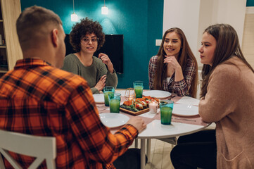 Group of friends enjoying dinner while sitting at the kitchen table together