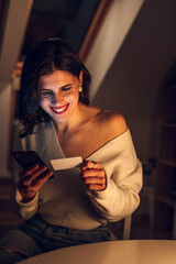 Woman using a smartphone and a credit while relaxing at home in the night