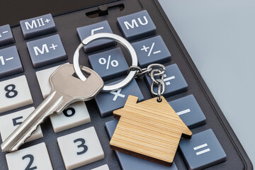 The concept of mortgage, sale and rental of housing and real estate. Mortgage credit lending. Calculator with keys and a keychain in the form of a house on a gray background. Copy space.
