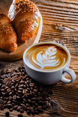 A cup of coffee and two croissants on an old wooden table
