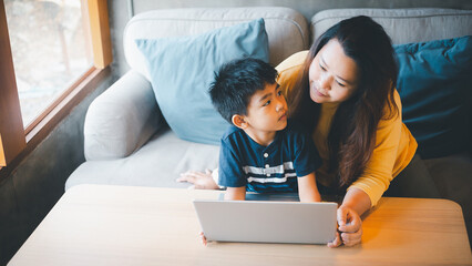 Mother and son watching something on screen while studying at a coffee shop using his laptop to study online during the COVID-19 lockdown. Online Education, Homeschool.