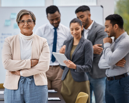 Leading her team towards greatness. Portrait of a mature businesswoman standing with her arms crossed in an office with her colleagues in the background.