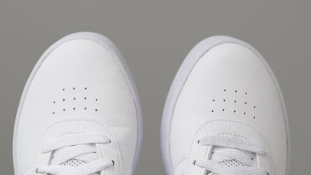close up video girls legs wearing white color sneakers and sitting in the bed and playing with feets moving from side to side, on white blanket. stay at home concept. stay safe. new sneakers.