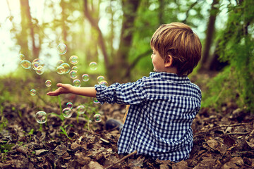 Fascinated by the magic of bubbles. Shot of a little boy playing with bubbles while sitting alone...