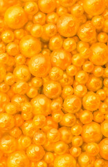 Beautiful background with pearl gold pearls, top view. Abstract texture for festive backgrounds. Shiny yellow surface of Christmas decorations. Gems close-up. Golden bright background.