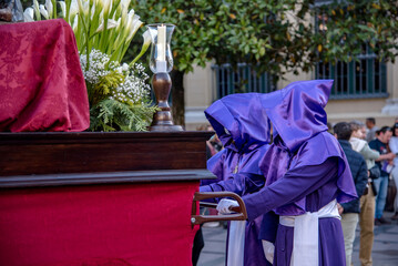 Detalle de los miembros de la cofradía de "El Descendimiento" vistiendo un hábito morado con capucha mientras empujan un paso en una procesión de Semana Santa en Valladolid.