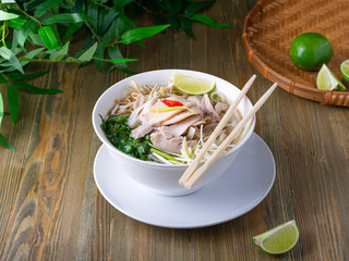pho bo spicy broth or soup in white ceramic bowl with rice noodles, beef slices and herbs. concept...