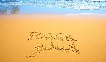 Concept or conceptual hand drawn thank you text carved in a golden sandy beach