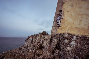 athletic dancer climbs fort wall on ocean cliff in Portugal