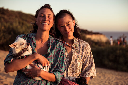 beautiful queer couple smile with dogs by ocean cliff in sunset