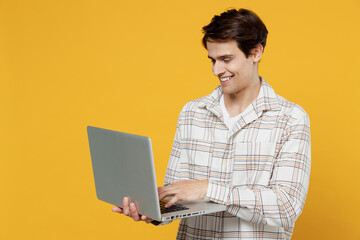 Young smiling happy copywriter freelancer caucasian man 20s wear white casual shirt hold use work on laptop pc computer isolated on plain yellow background studio portrait. People lifestyle concept