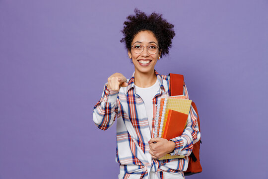 Young cool girl woman of African American ethnicity student in shirt backpack point index finger camera on you say do it isolated on plain purple background. Education in high school college concept.