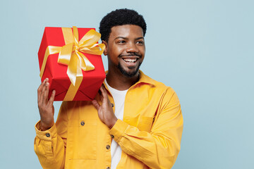 Young man of African American ethnicity wear yellow shirt hold red present box with gift ribbon bow...